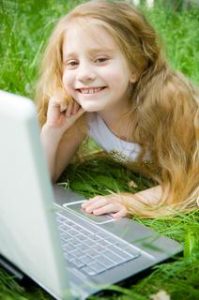 Smiling little girl with laptop in green grass